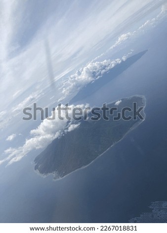 Shot view of Mount Maitara and Ternate, cloud, air, and sea from inside the plane