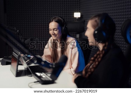 Female host and guest sitting at table with equipment while broadcasting radio program in recording studio