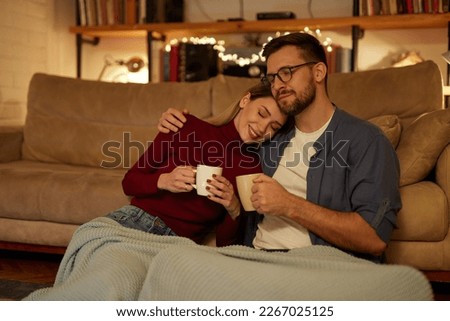 Young couple drinking tea while sitting in the living room at night
