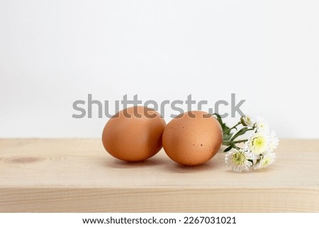 Brown eggs lie on a natural wooden board on a white background. Easter picture two eggs and a chamomile flower.