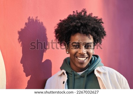 Close up portrait photo of young stylish happy African American cool hipster guy face laughing on red city wall lit with sunlight. Smiling cheerful cool gen z male model standing outdoors. Headshot. Royalty-Free Stock Photo #2267032627
