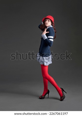 Vogue model in preppy outfit and red cloche hat striking a pose isolated on gray background