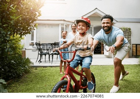 Learning, bicycle and proud dad teaching his young son to ride while wearing a helmet for safety in their family home garden. Active father helping and supporting his child while cycling outside Royalty-Free Stock Photo #2267074081