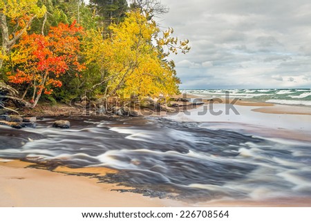 Long exposure shows the whitewater of the Hurricane River flowing across a beach and into Lake Superior surf on a cloudy day at Pictured Rocks National Lakeshore in Michigan's Upper Peninsula.