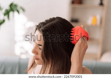 Girl enjoys doing herself a head massage using a scalp massager. Royalty-Free Stock Photo #2267092001