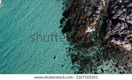 Drone photo of blue water surface with little rocks on the side. Aerial picture of shallow water in Dunsborough, South-west Australia. Ocean and rocks with small waves and foamy water.