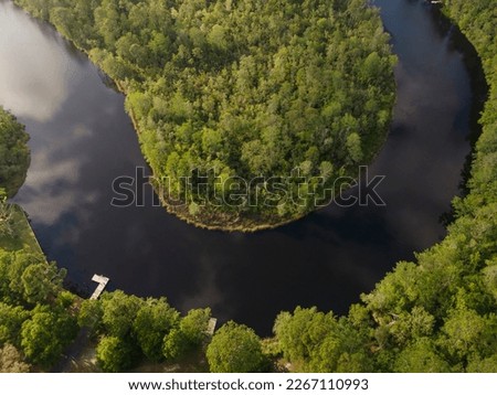 U-shaped waterway of a river passing through the green forest in Navarre, Florida. There are docks at the bottom on a river with reflections of the sky in an aerial shot view.