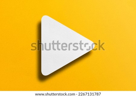 White paper cut into triangle shape, play button set on yellow paper background. Royalty-Free Stock Photo #2267131787