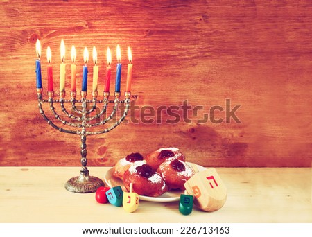 jewish holiday Hanukkah with menorah, doughnuts and wooden dreidels (spinning top). retro filtered image 