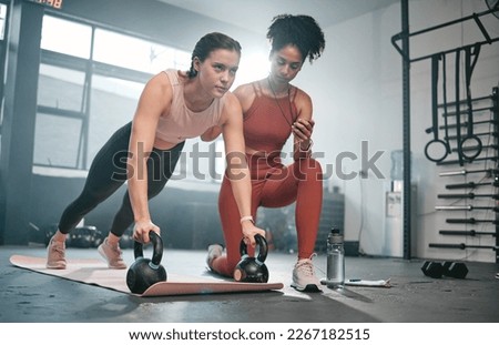 Personal trainer, kettle bell and stopwatch with a black woman coaching a client in a gym for her workout. Health, exercise or training and a female athlete doing a plank with her coach taking time Royalty-Free Stock Photo #2267182515