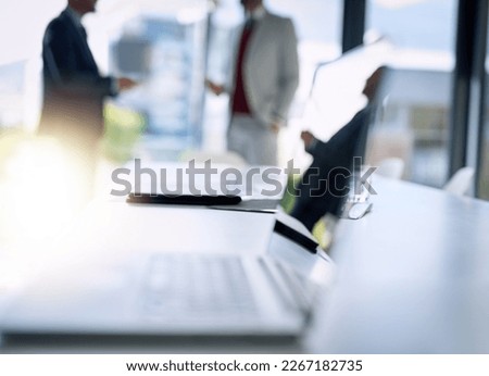 Business in focus. Shot of an open laptop on a boardroom desk with two businessmen blurred in the background.
