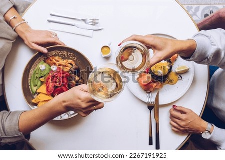 Friends holding a glass of wine and toasting. Top view of brunch table. Royalty-Free Stock Photo #2267191925