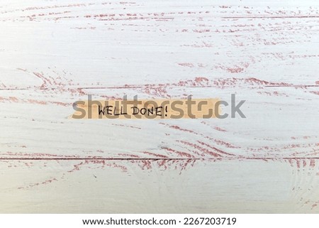 motivational message 'well done' handwritten on colorful washi tape against white wooden background