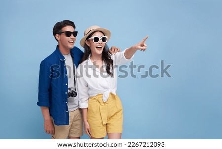 Happy Asian couple tourist hand pointing to copy space with going to travel on holidays isolated on blue background. Royalty-Free Stock Photo #2267212093