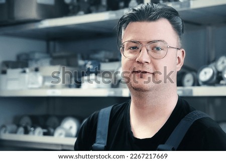 Portrait of white Caucasian man with glasses in production workshop against background of racks with instruments, sensors and pressure gauges. Worker of control and measuring service.. Royalty-Free Stock Photo #2267217669