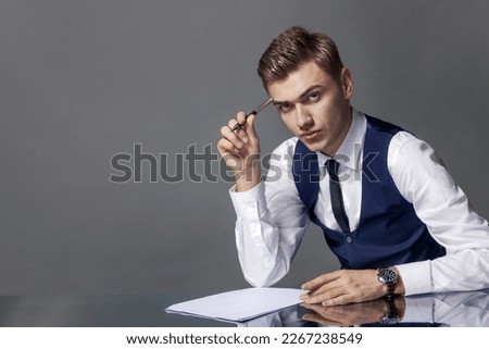 A man in a suit at a writing desk with a pen isolated on a gray background, studio.