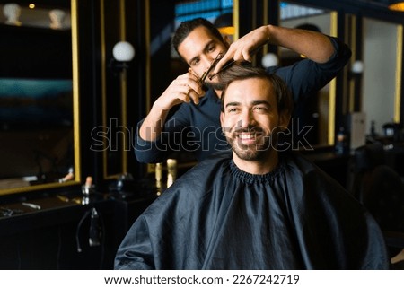 Attractive happy man smiling while getting a new trendy haircut or hairstyle with a professional male barber Royalty-Free Stock Photo #2267242719