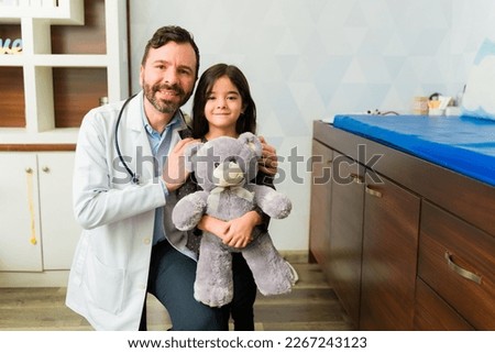 Cheerful caucasian doctor hugging a beautiful little child with a teddy bear coming to the doctor's office  Royalty-Free Stock Photo #2267243123