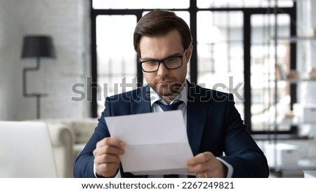 Focused business leader in formal suit and glasses reading letter, receiving official document, bank or insurance notice, contract, agreement, certificate, invitation. Paperwork, mail concept Royalty-Free Stock Photo #2267249821