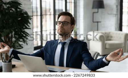Peaceful business leader meditating at workplace, making zen hands and fingers at laptop. Calm businessman relaxing in office, breathing, doing yoga, practicing mindfulness and stress relief exercises Royalty-Free Stock Photo #2267249833