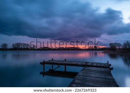 View from a wooden pier on a calm lake during sunset with dark rainy clouds
