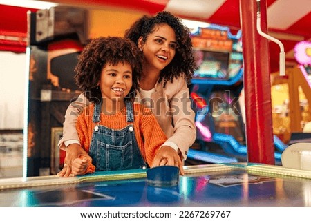 A cute African-American child with afro curls with her mother playing air hockey at an amusement park and carousel on her day off in the evening. Royalty-Free Stock Photo #2267269767