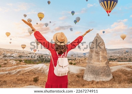 On a summer day in Cappadocia, Turkey, the girl in her pretty dress finds herself mesmerized by the elegant sight of air balloons in the sky.