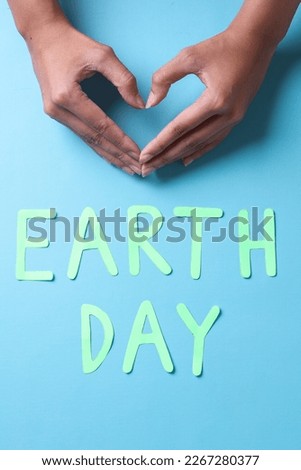 Earth day lettering and fingers forming heart shape isolated on blue background. World earth day concept. 