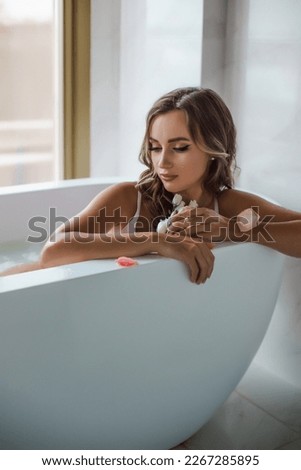 Attractive girl relaxes in a bath on a light background with rose petals