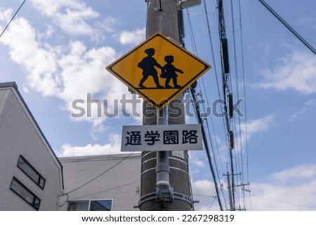 This photo shows a road sign indicating a Japanese-style pedestrian crossing and school route against a clear blue sky.