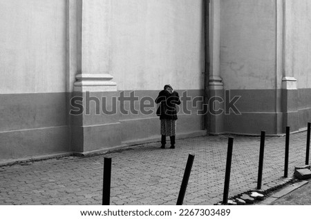 A poor woman standing in front of a wall with her head down, back view	