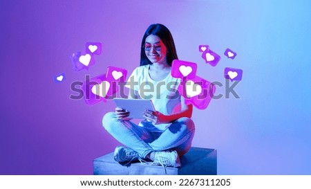 Smiling young asian woman in glasses typing on tablet, has romantic chat with hearts on neon background, studio, panorama. Dating app remotely, love and relationships at Valentine day, new normal Royalty-Free Stock Photo #2267311205