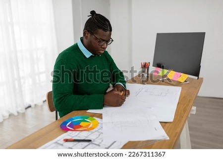 African American Male Designer Working Drawing A Plan Using Color Palette Sitting Near PC Computer In Modern Office, Wearing Eyeglasses. Successful Web Design Career Concept. Side View Shot