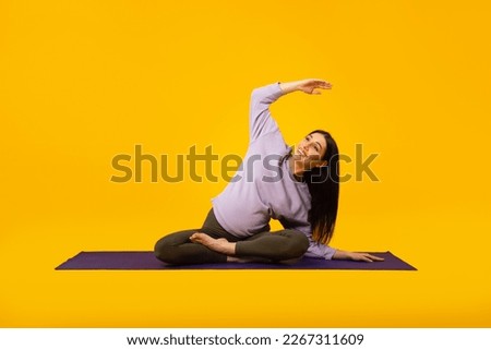 Active pregnancy concept. Happy future mom doing her morning yoga workout on mat over yellow studio background. Pretty expectant woman doing domestic fitness, exercising indoors