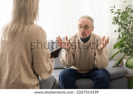 Senior man patient and young woman caregiver medical worker in uniform hold clipboard noting personal information talking listens client telling about health complaints, care support nursing concept Royalty-Free Stock Photo #2267314339