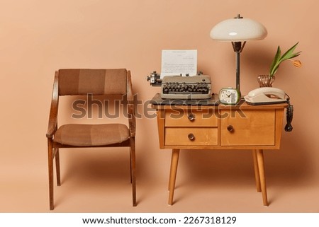 Horizontal shot of old wooden chair table with typewriter lamp stationary telephones and clock with no people against brown background. Old furniture. Vintage style