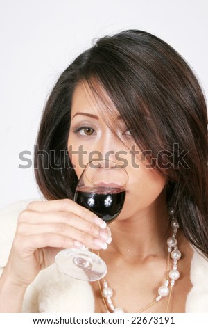 Elegant woman drinking from a glass of red wine and wearing a fur jacket and beads