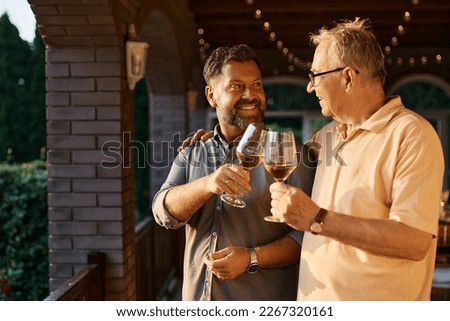Happy senior man and his son toasting with wine during family gather on a terrace. Royalty-Free Stock Photo #2267320161