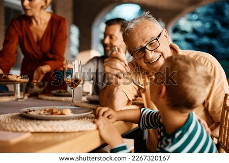 Happy grandfather having fun while feeding his grandson at dining table.  Royalty-Free Stock Photo #2267320167