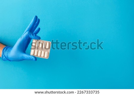Doctor's hand in blue glove holds pills in glister on light blue background. The concept of medical treatment of diseases, writing prescription