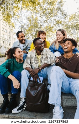 Vertical shot of happy multi-ethnic group of young hipster diverse student friends having fun together while hanging out sitting together outdoors. Friendship concept