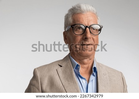 portrait picture of handsome man in his 60s with glasses looking away, wearing elegant suit with open collar shirt and posing on grey background