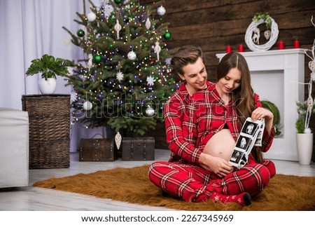 A man and a pregnant woman look at ultrasound images while sitting on a carpet.