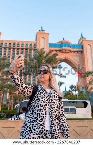 stylish tourist wearing dark glasses, taking in the sights of Dubai. Her modern fashion sense reveals her self-assured nae and readiness to explore new places. She poses in front of  fuistic building
