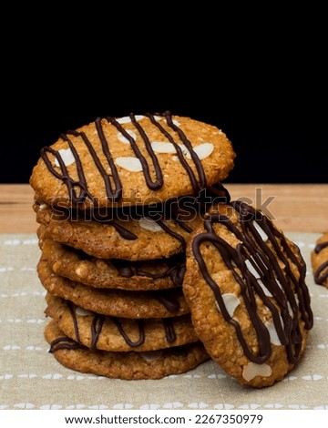 Oatmeal cookies stacked on kitchen towel, wooden table and black background, vertical photo
