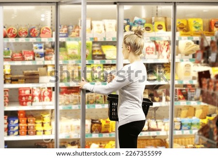 Woman choosing frozen food from a supermarket freezer, reading product information Royalty-Free Stock Photo #2267355599