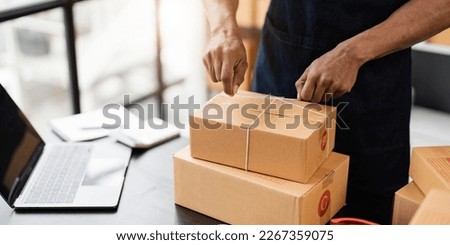 Photo of young entrepreneur man packing he goods while sitting in table comfortable sitting room as background. Shipping, Shopping online, Small business entrepreneur, SME, freelance.
