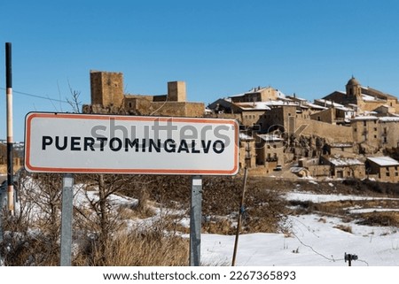 Road sign of the Puertomingalvo town, with the snow-capped town behind
