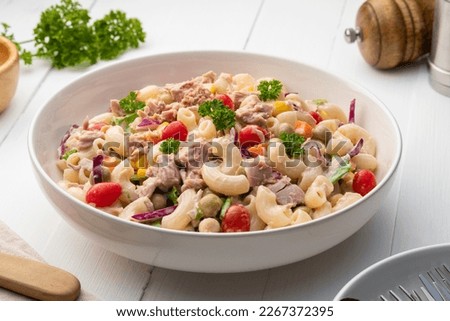 Homemade macaroni salad with elbow pasta and canned tuna, carrot, Purple cabbage, corn, tomato, green peas and mayonnaise dressing in a white plate on wooden table. Royalty-Free Stock Photo #2267372395