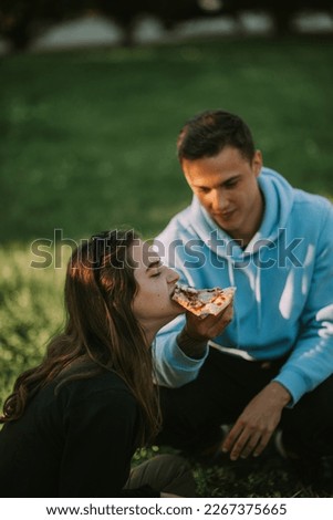 Handsome boy feeding  his girlfriend  with pizza slice whil sitting at the park